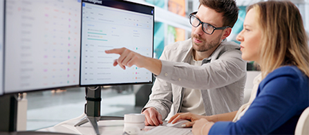 Professionals collaborate at a desk, reviewing digital information displayed on a large monitor. 