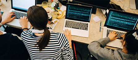An overhead view of a team working together at a workstation equipped with laptops and monitors. 
