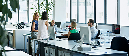 A group of professionals sit and stand around an office space while chatting.