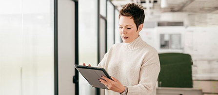 Businessperson using a tablet while standing in a modern office workspace. 