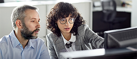 Image alt Text: Two colleagues reviewing information on a computer monitor while working together in an office. 