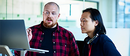 Two colleagues reviewing information on a laptop in an office workspace. 