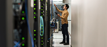 IT technician standing at end of rows of servers examining equipment in data center. 