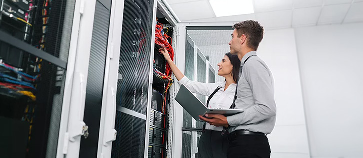 Two IT professionals inspect network cables and equipment in a data center.