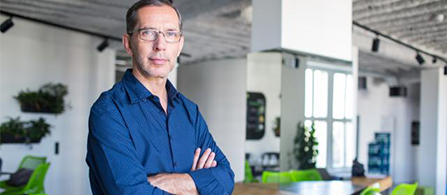  Businessperson looking directly into camera with hands crossed standing in open aired office vestibule.