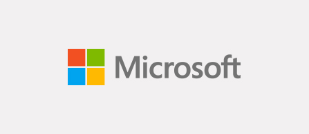 The Microsoft logo on a light gray background. A four-square emblem in red, green, blue, and yellow sits to the left of the word “Microsoft” written in gray lowercase lettering.