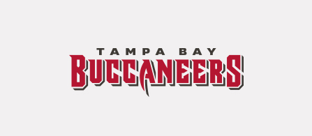 The Tampa Bay Buccaneers logo: 'TAMPA BAY' in small dark letters above 'BUCCANEERS' in bold red block capitals, accompanied by a red pennant flag bearing a sword, on a white background.