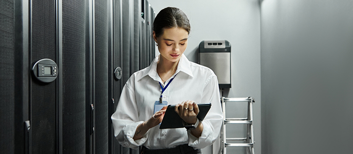 A person works on a tablet device in a server room.