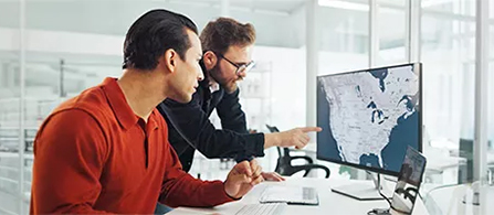 Two business professionals in a white office setting look intently at a computer monitor displaying a map of the United States of America.