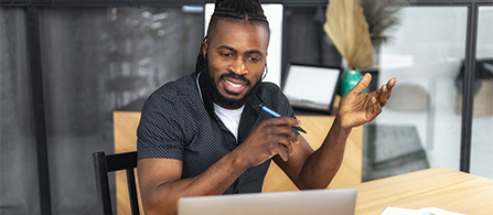 One business professional sits at a desk with their hands raised in a conversation gesture, while talking to their laptop screen.