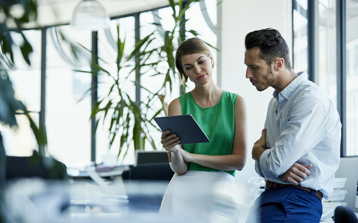 A woman and man in business attire look at a tablet screen.