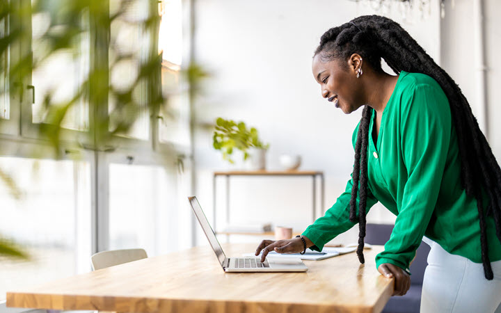 A woman standing at a desk in an office while using her laptop.