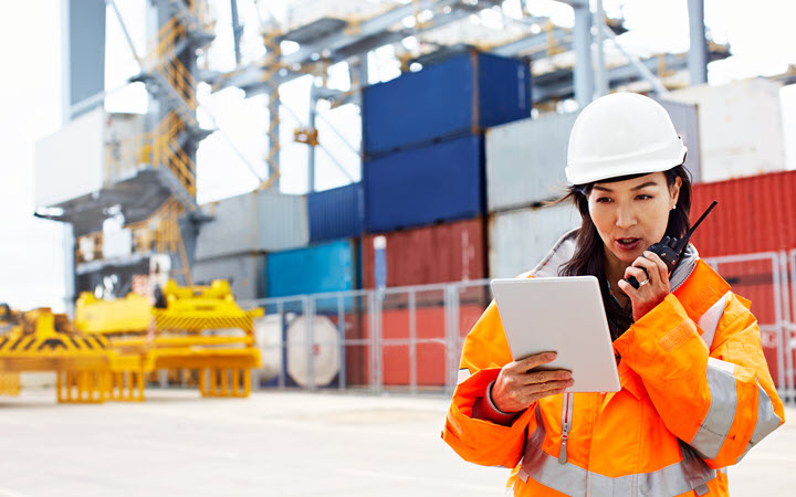 A woman in a factory wearing business attire and working on a tablet computer