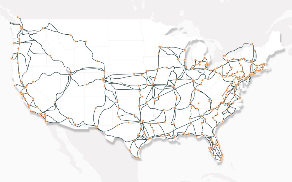 A map of the United States showing a dense network of orange and dark gray lines connecting dozens of orange dot locations across the country, with heavier concentration in the eastern half and along major corridors, on a light gray background.