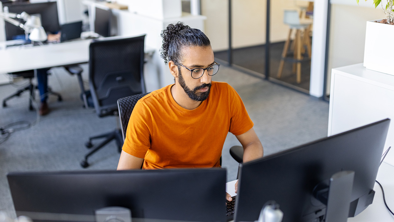 Person working at a desk with two computer monitors in a modern office.