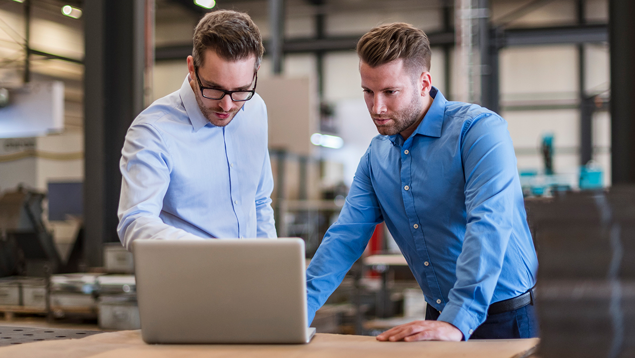 Two engineers in data center standing at desk reviewing information on a laptop. 