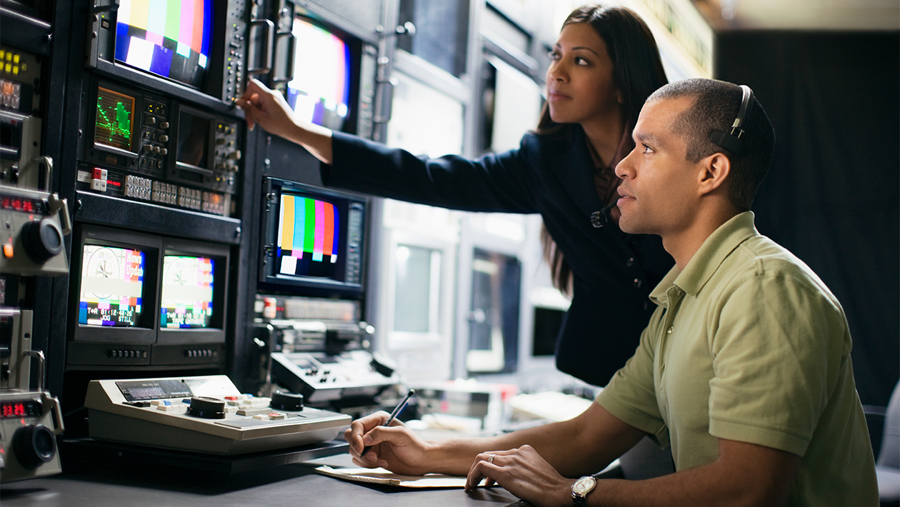 Two broadcast engineers in production booth reviewing and calibrating audio-visual color bars signals
