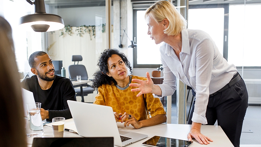 Group of colleagues collaborating at a conference table while reviewing information on a laptop in a modern office. 