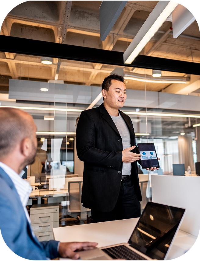 A man showcasing a data visualization on his tablet in an open-office setting.  